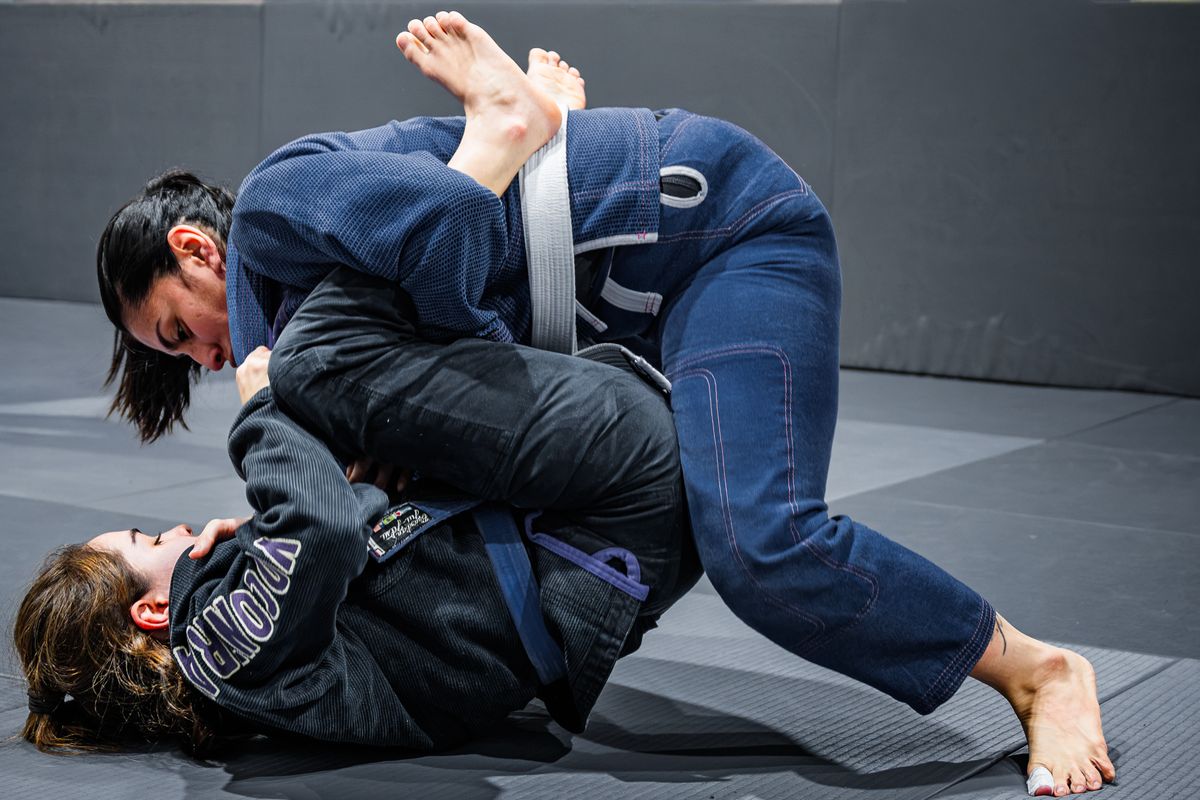 Two practitioners in dark gis grappling on the mats
